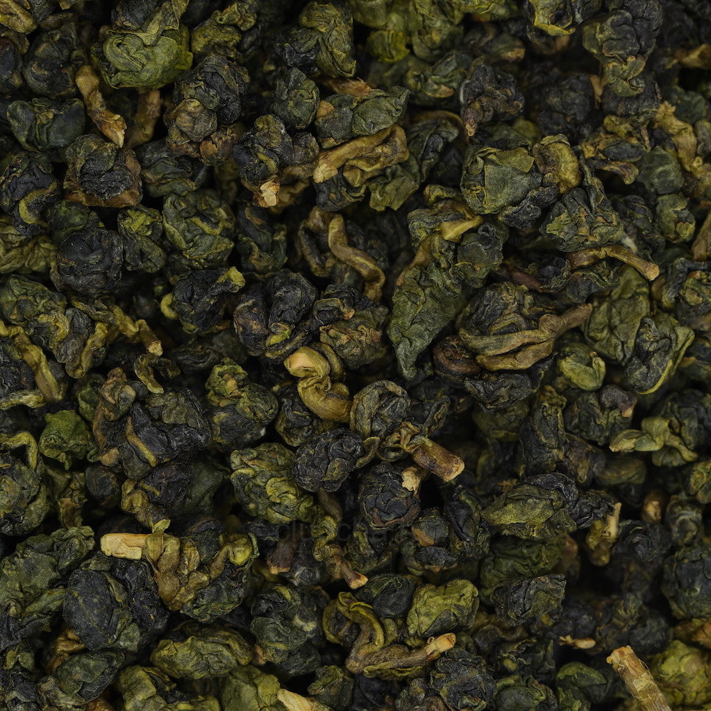 Tightly rolled green oolong tea leaves with a soft jade hue, representing Ming Yue Cui Xiang – Jade Fragrance of Bright Moon, captured in a top-down view on a clean surface.